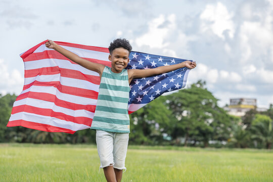 American children boy holding waving american USA flag running and having fun in the grass and happily on independence day.