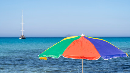 Isolated green, red, blue and yellow beach umbrella. Blue sky. Relaxing context. Summer holidays at the sea. General contest and location. Turquoise sea in the background. Multicolor umbrella