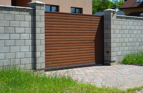 A horizontal wooden slat automatic sliding gate, driveway sliding gate with a brick fence, and paver driveway.