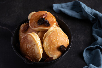 Honey almond raisin pancakes in a black pan on a black background.