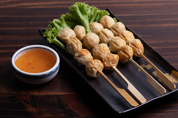 Grilled meatballs on skewers in a black plate with spicy dipping sauce