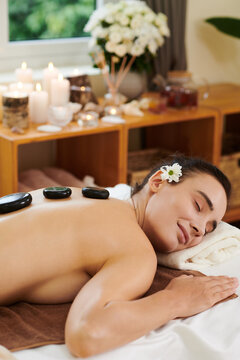 Beautiful young woman relaxing with her eyes closed during stone therapy in spa salon