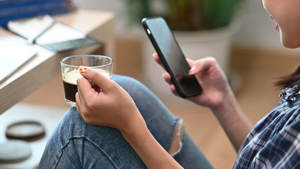 Young woman holding coffee cup and using smart phone at home.