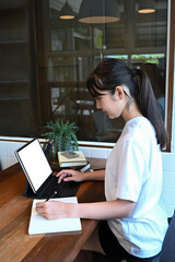 Side view of young female student studying online with tablet at home.