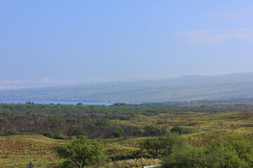 Fototapeta premium ハワイ島（ビッグアイランド）。緑の草に覆われた溶岩の大地と海に太陽の光が降り注ぐ。