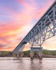 Johnsons Crossing, Teslin River steel Bridge on the Alaska Highway during spring summer time with cloudy, pink sunset sky and magnificent, huge structure over the flowing water below. 