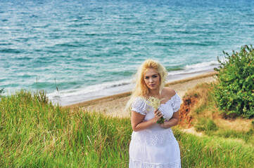Fototapeta na wymiar Young blonde woman in nature . A girl in a white dress on the seashore