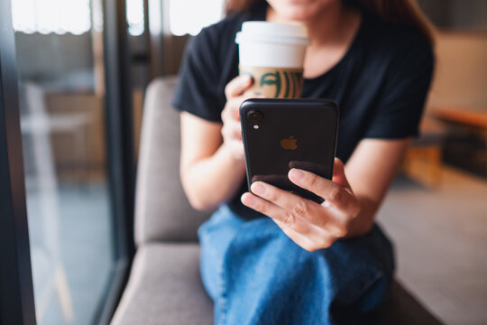 Jun 16th 2021 : A woman holding and using Iphone XR smart phone while drinking coffee at Starbucks coffee shop, Chiang mai Thailand