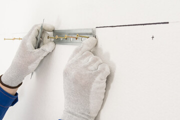 a worker attaches fasteners to a white wall for hanging kitchen cabinets, close-up