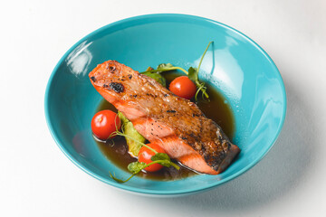 Fish steak with cherry tomatoes and soy sauce served in a blue bowl over white background.
