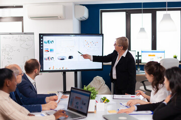 Senior woman company leader brainstorming in conference room Corporate staff discussing new business application with colleagues looking at screen