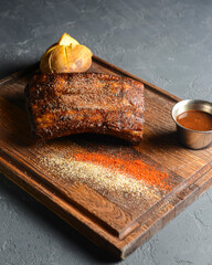 Grilled pork ribs with baked potato and sauce on a wooden board over stone grey background.