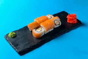 Philadelphia Maki Sushi made of Fresh Raw Salmon, Cream Cheese and Cucumber served on a black board over blue background