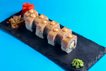 Japanese sushi with eel, wasabi sauce and pickled ginger served on a black board over blue background.