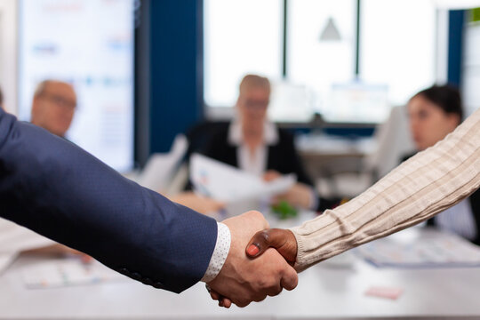 Close up of multiracial business partners standing in front of conference desk shaking hands after signing partnership contract. Diverse team being happy for successful negotiations in startup company