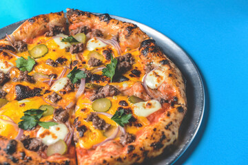 Whole cheese and meat pizza over blue background. Pizza with onions and pickles served on a metal tray.