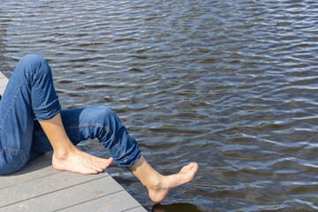 A man dips his feet in the water on the pier