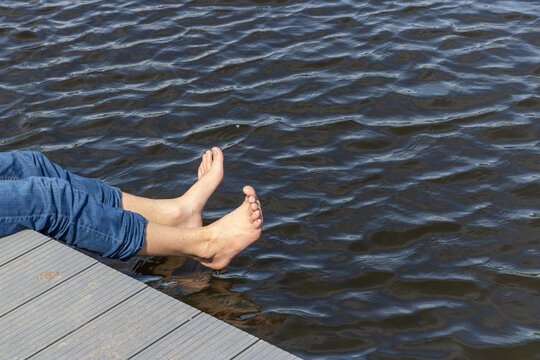 Legs And Bare Feet Of Man Dangling Over Water