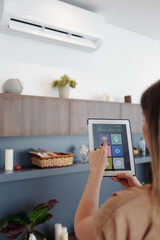 Young woman using smartphone home application on tablet computer when setting temperature in her apartment