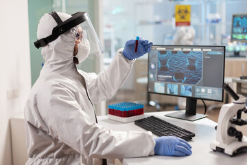 Doctor conducting experiment in lab holding vaccutainer dressed in ppe suit. Medical team examining vaccine evolution in medical lab using high tech and chemistry tools for scientific research.