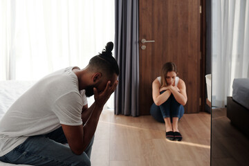 Fototapeta na wymiar Unhappy offended husband and wife sitting in bedroom apart from each other after big quarrel or fight, divorce and relationship problems concept