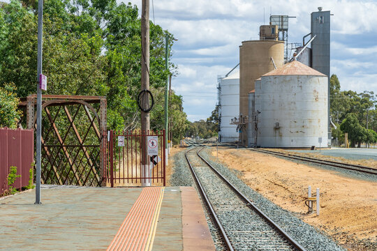Looking along a rural railway platform, down the railway line at grain silos