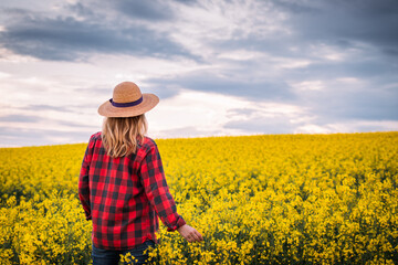 Female farmer standing in rapeseed field. Agronomist inspecting blooming oilseed rape field at springtime