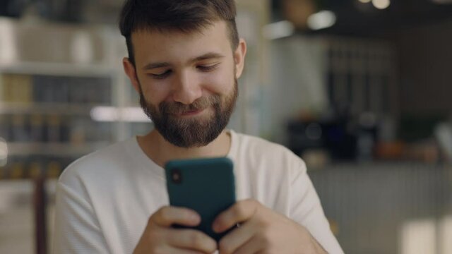Smiling bearded guy with smartphone relaxing at cafe