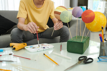 Teenage boy painting styrofoam balls when making model of Solar System for school