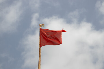 Red flag waving on a background with blue sky and white clouds. Red flag raised to prohibit swimming due to waves on the beach.
