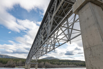 Large steel structure bridge in northern Canada in artistic style with blue sky clouds in the background. Taken from underneath the magnificent transport bridge. 