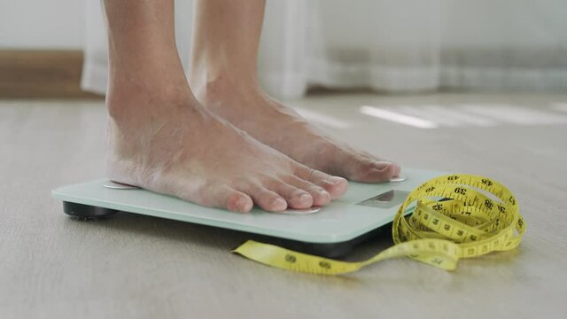Woman foot stepping on weigh scales with tape measure. A woman is weighing herself after following a diet program and course. Diet Concept and loss weight.

