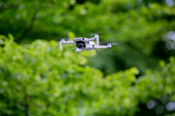 Drone in flight, green trees in the background, selective focus on drone - Powered by Adobe