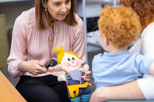 child health nurse demonstrating otoscope on toy to little boy