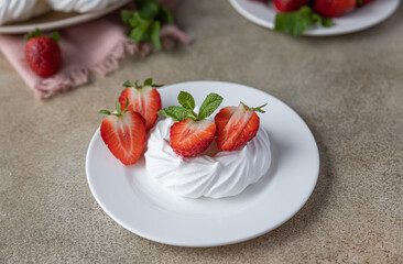 Mini Pavlova meringue cakes with strawberries and mint on a plate, concrete background.