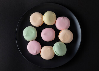 Top view of colorful marshmallows on black plate on dark background.