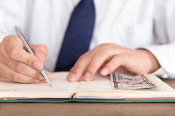 Fototapeta premium Man jot down things and some dollar banknotes in his notebook