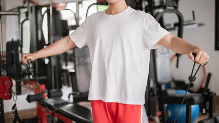 Training gym concept a male teenager using a gym equipment pulling his both muscular arms against...