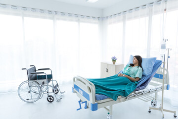 Inattentive young Asian female patienit with hospital clothes feels unhappy, bad, sad . She is thinking about medical diagnosis, surgery and treatment on hospital bed in white room, hospital.