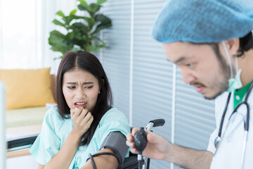 Obraz premium Smart male doctor is going to take funny female patient's blood pressure on the wheelchair by using medical equipment (Sphygmomanometer) in hospital.