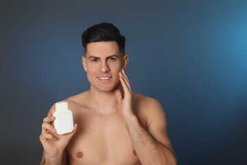 Handsome man holding post shave lotion on blue background