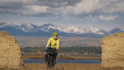 The man travel on mixed terrain cycle touring with bikepacking. The traveler journey with bicycle bags. Sport bikepacking, bike, sportswear in green black colors. Mountain snow capped, stone arch.