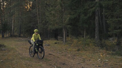 The woman travel on mixed terrain cycle touring with bike bikepacking outdoor. The traveler journey with bicycle bags. Stylish bikepacking, bike, sportswear in green black colors. Magic forest park.