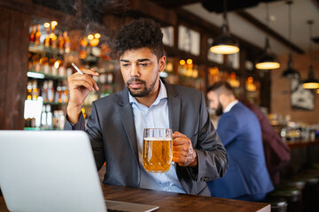 Man drinking beer and smoking cigarette while working on computer. Bad habit concept.