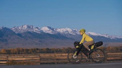 Obraz premium The woman travel on mixed terrain cycle touring with bikepacking. The traveler journey with bicycle bags. Sport tourism bikepacking, bike, sportswear in green black colors. Mountain snow capped.