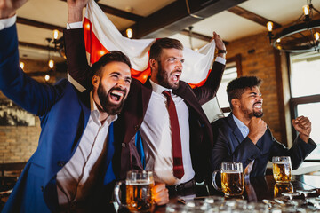 Men fans screaming and watching football on TV and drink beer in a pub