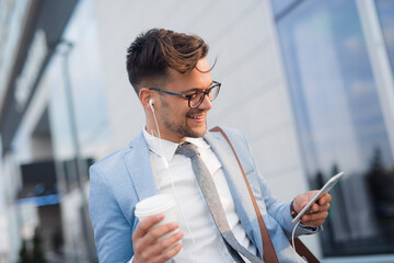 Smiling businessman holding earphones and cup of coffee