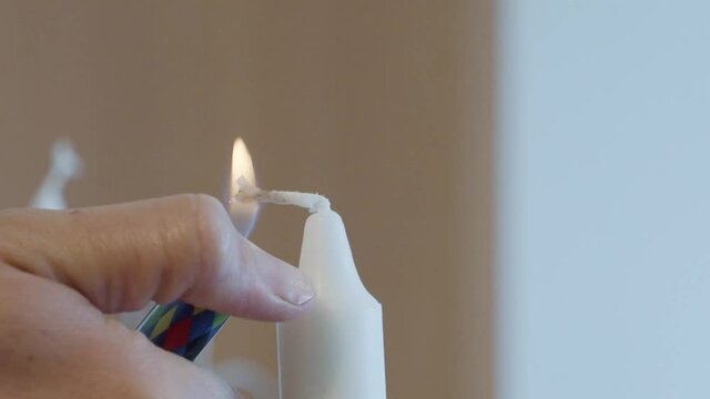 Close-up of girl's hand lighting a candle. A woman uses a lighter to light a couple of candles for the dining table.