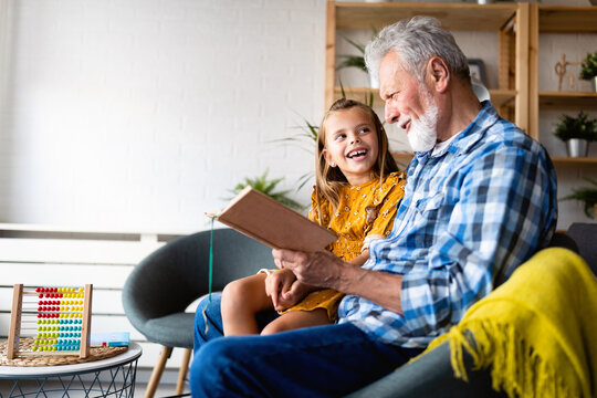 Happy little girl with grandfather reading story book at home