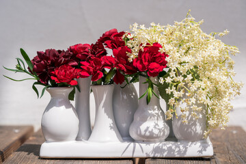 beautiful red carnation blossoms with elder flowers in a white flower vase on the balcony on a sunny summer day